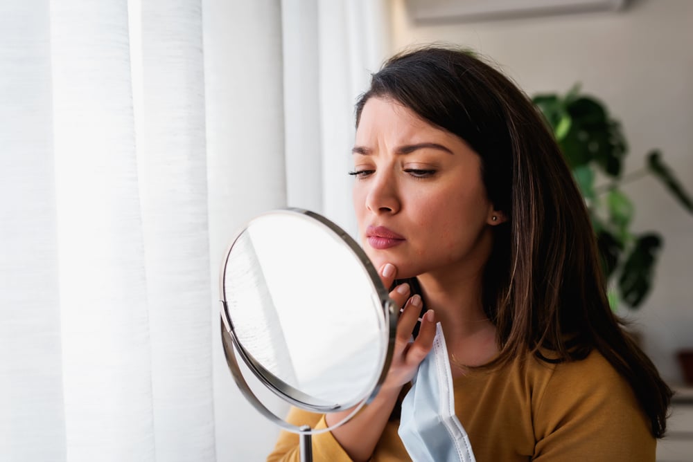Woman looking in the mirror at her acne scars needing Sculptra in Littleton, CO